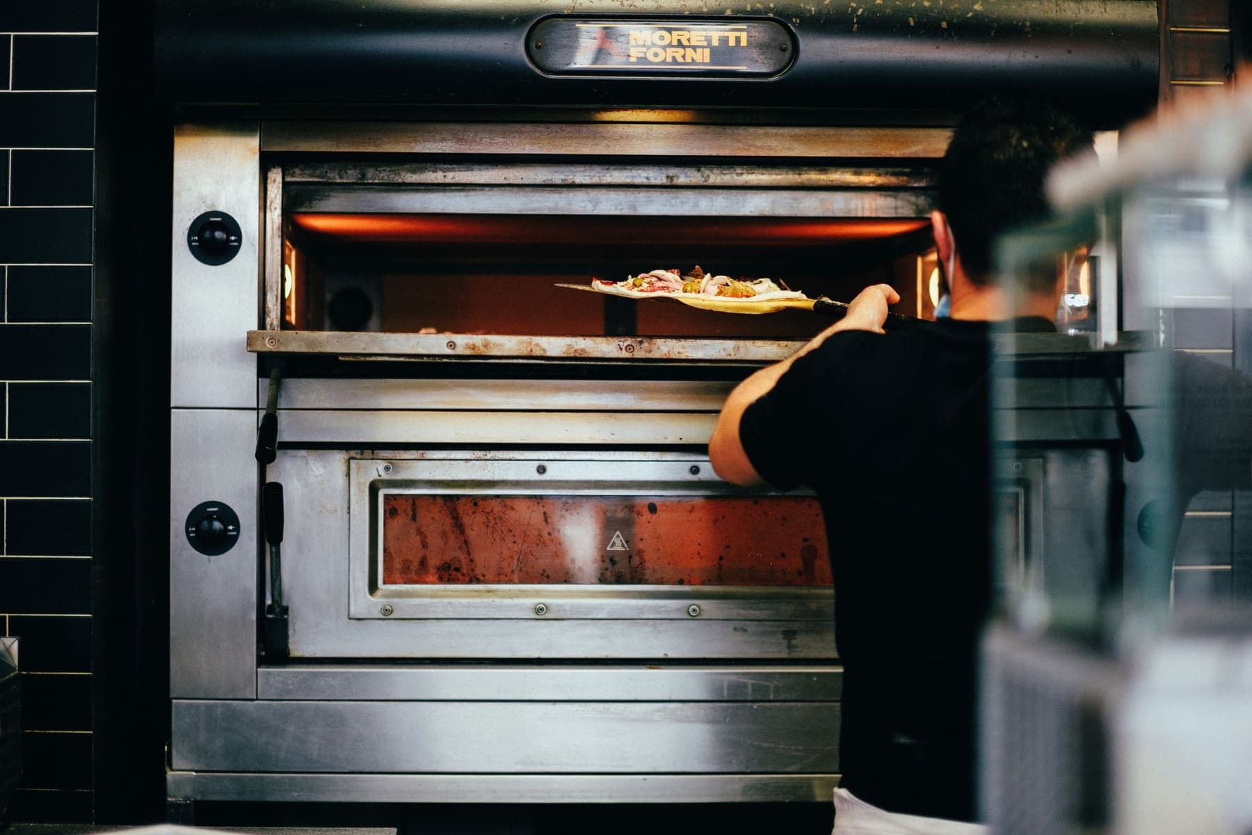 Pizzaiolo retirando uma pizza de um forno de lastro Moretti Forni em uma cozinha profissional