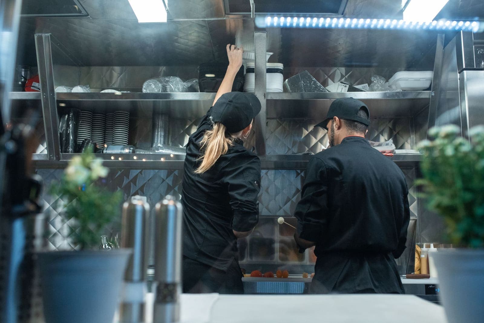 Equipe trabalhando em uma cozinha profissional com bancadas e equipamentos em aço inox
